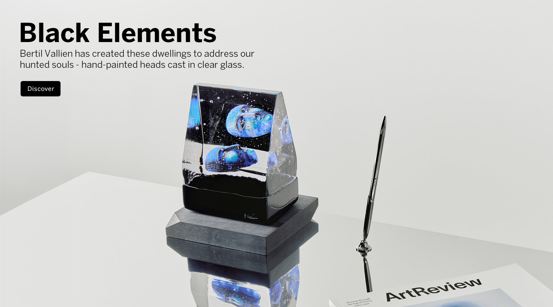 Artistic glass sculpture with hand-painted heads on a white background, featuring text about Black Elements and Bertil Vallien.
