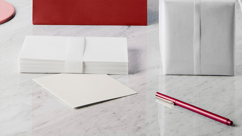 White gift wrapped package with white stationery set and a red pen on a marble surface