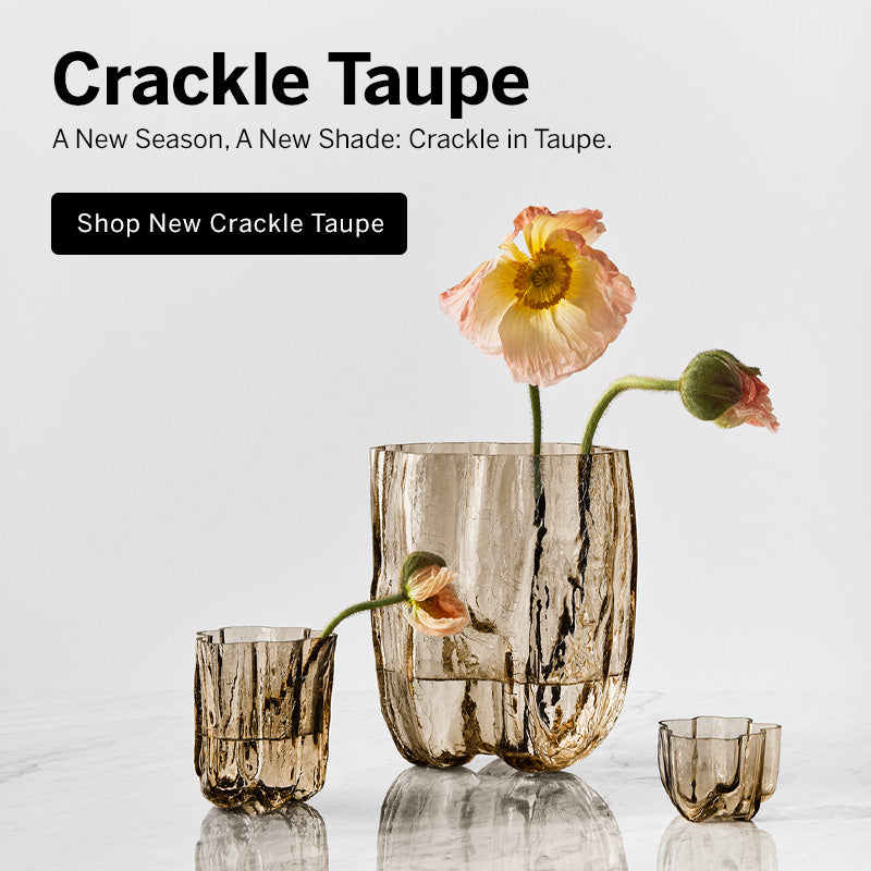 Mobile version image of Crackle collection taupe vases and small votive on a marble surface with flower stems in the vases and a light background with text introducing new taupe color for Crackle collection.