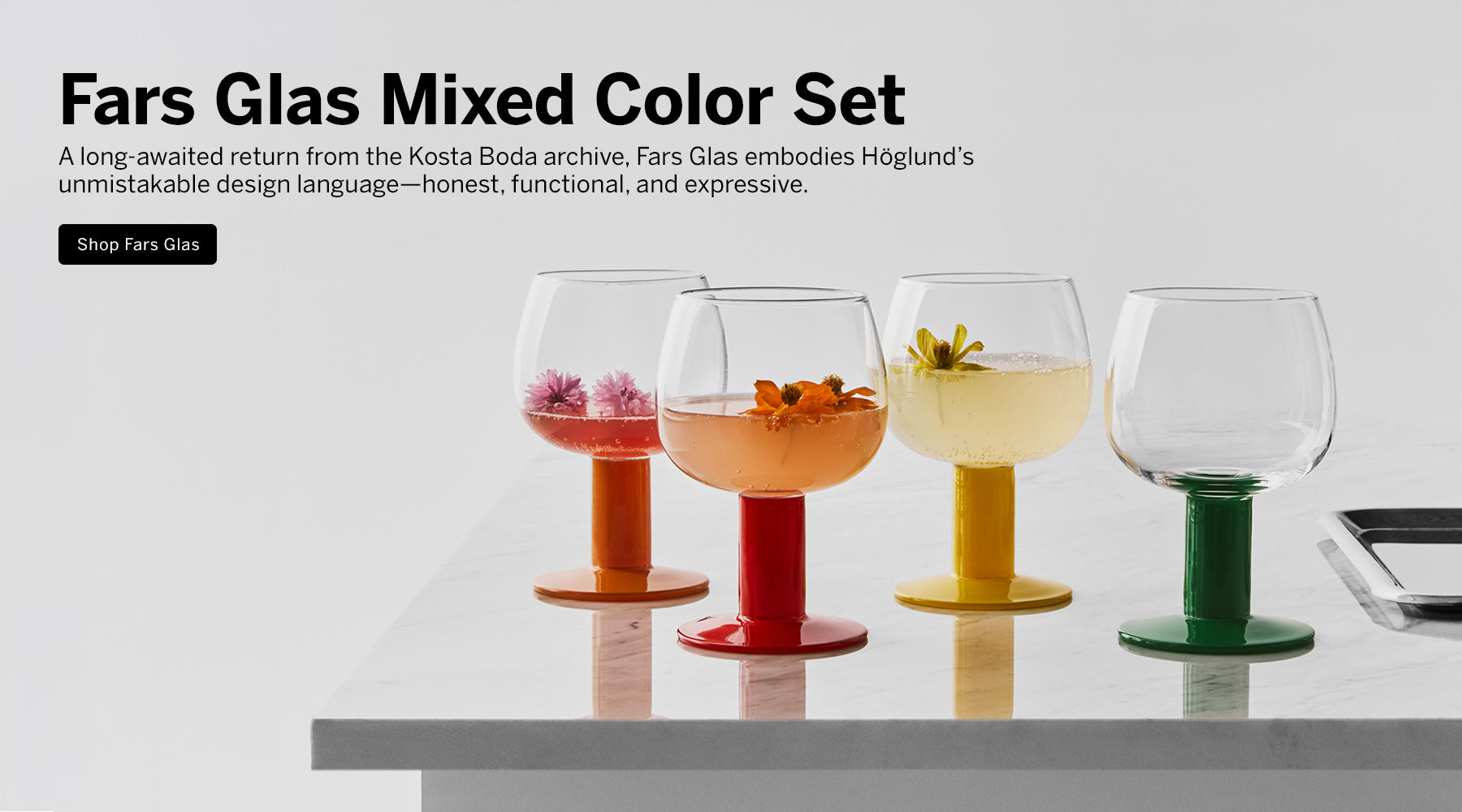 Four Fars Glas mixed-color stemware glasses with orange, red, yellow, and green bases, shown on a white surface against a light gray background with promotional text; 'A long-awaited return from the Kosta Boda archive, Fars Glas embodies Höglund’s unmistakable design language—honest, functional, and expressive.'