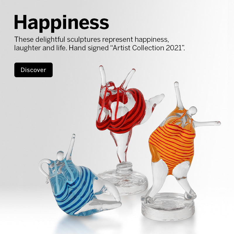 Mobile version image of three Happiness Collection colorful crystal sculptures of robust women in bathing suits on a white surface against a white background, with a wooden block and two books beside them. Text on the left reads 'Happiness' and references the Artist Collection 2021.