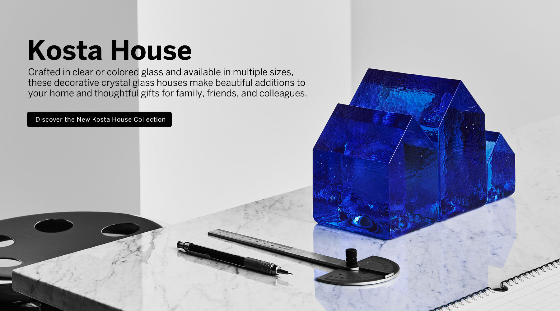 Kosta House collection feature 3 blue crystal house-shaped sculptures on a marble surface with mechanical pen  and measuring instrument with text about discover the Kosta House collection.