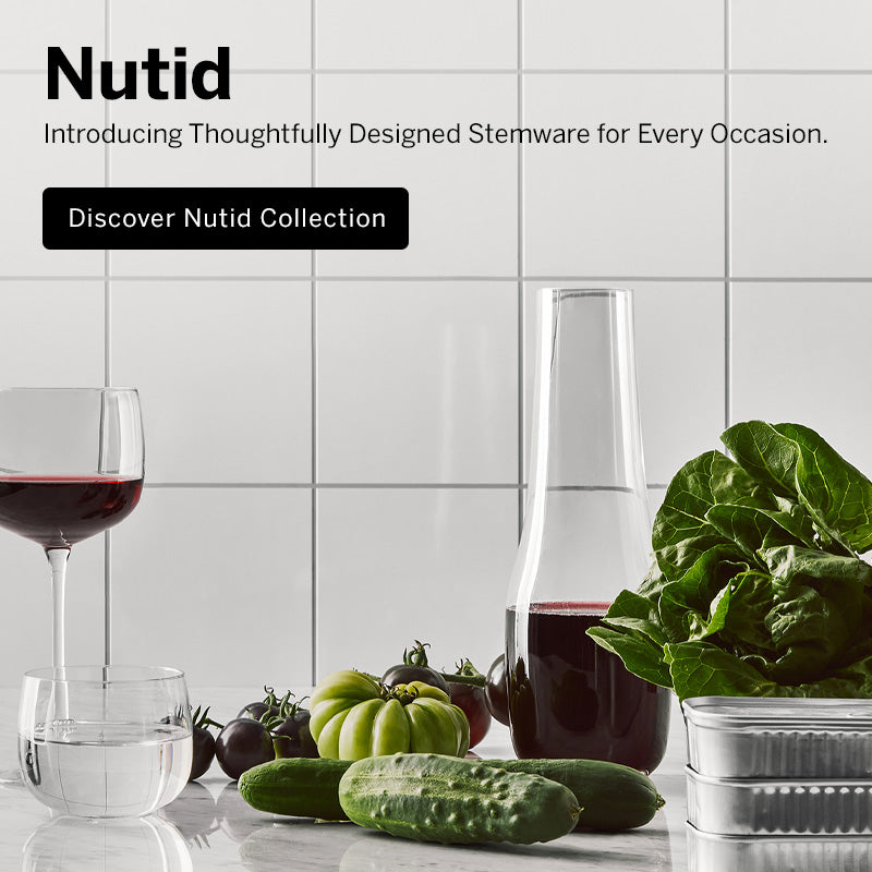 Mobile version image of Nutid collection crystal decanter, wine, coupe, apertif, and tumbler glasses on white marble kitchen counter surface with vegetables and a white tile background with text saying 'Introducing Thoughtfully Designed Stemware for Every Occasion, Discover Nutid Collection'.