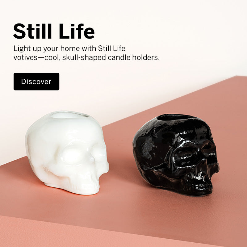 Mobile version image of Still Life collection skull shaped white and a black votive candle holder on a peach colored surface and a light background with text promoting Still Life collection.