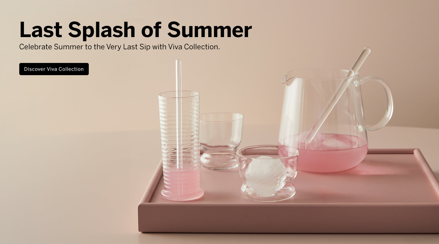 Viva collection crystal pitcher filled with pink liquid and a crystal mixing stick in it sitting on a pink tray beside a ribbed Viva tumbler glass with a crystal straw, a small clear Viva DOF glass, and a round ice in the glass, against a warm beige background with promotional text 